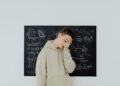 Teenager standing in front of a blackboard with math equations, covering his face in frustration.