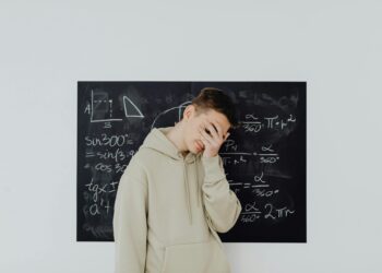 Teenager standing in front of a blackboard with math equations, covering his face in frustration.